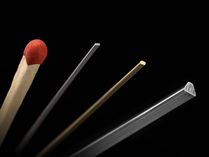 Matchstick next to several metal profiles with different cross sections on a black background